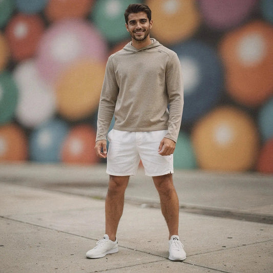 Man wearing beige slim fit hoodie and white shorts, standing outdoors, colorful mural in background