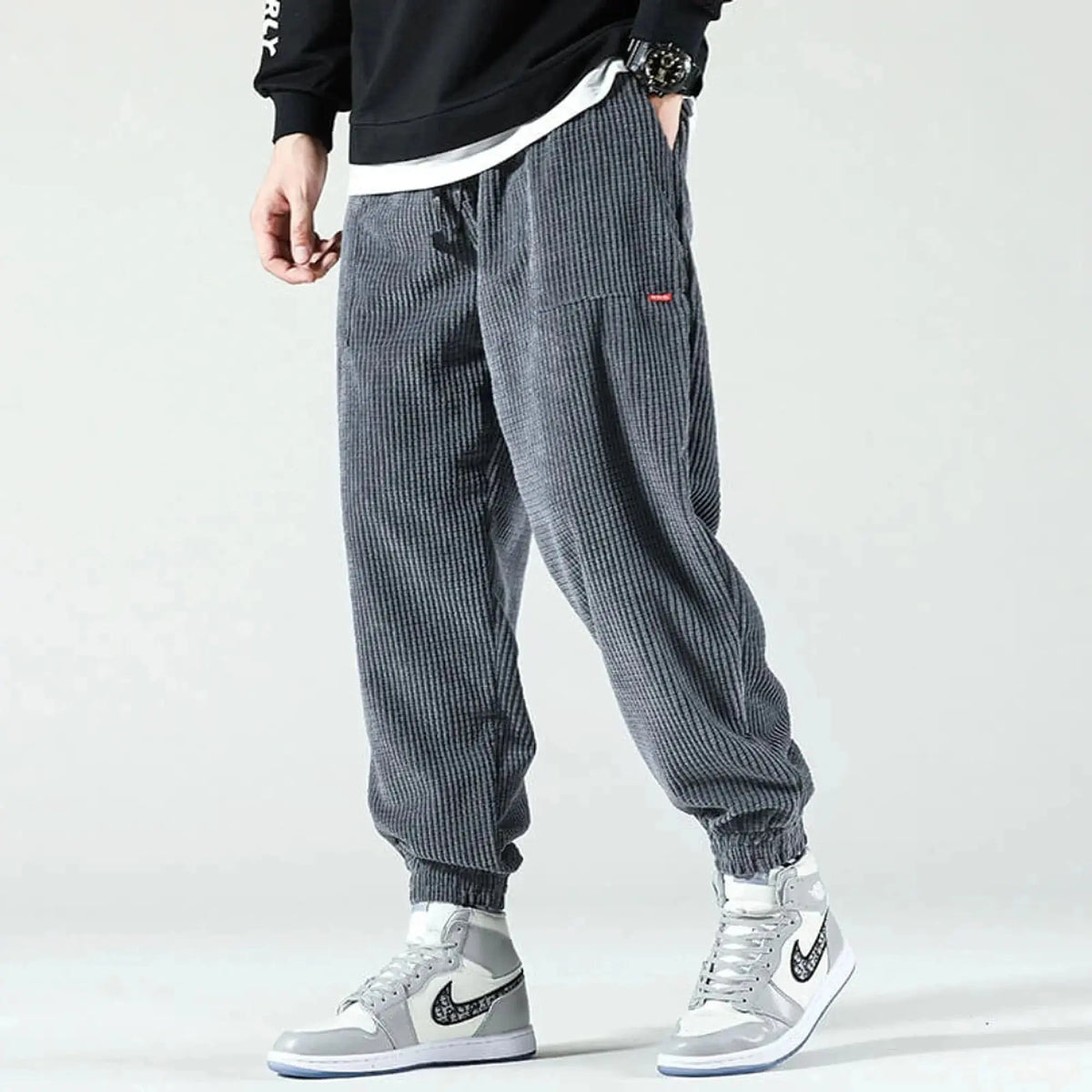 Man wearing grey corduroy joggers with elastic cuffs, standing sideways, paired with high top sneakers