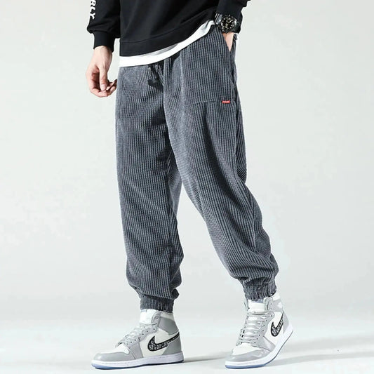 Man wearing grey corduroy joggers with elastic cuffs, standing sideways, paired with high top sneakers