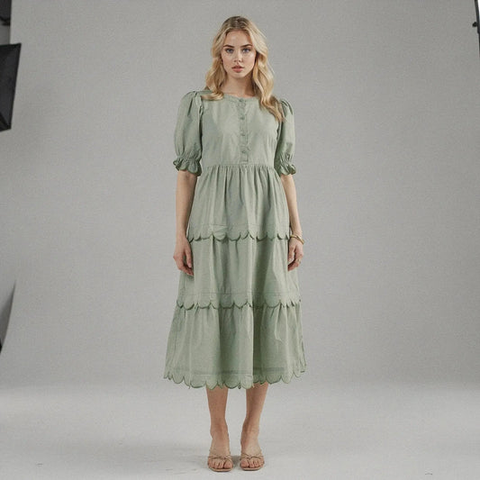 Woman wearing a light green A line midi dress with scalloped hem, standing facing on plain background