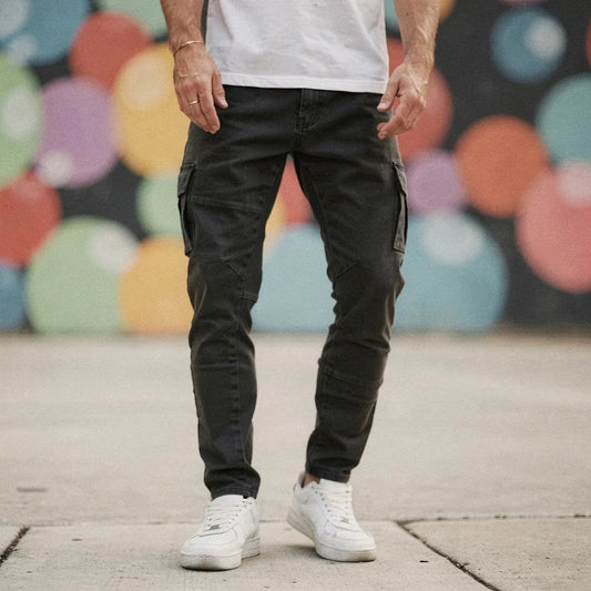 Man wearing dark grey slim fit cargo trousers with pockets, standing on pavement, colorful wall behind