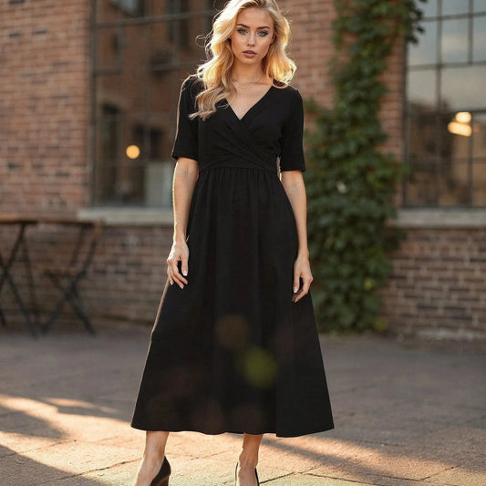 Woman wearing a black V neck midi dress with short sleeves, standing outdoors against a brick wall